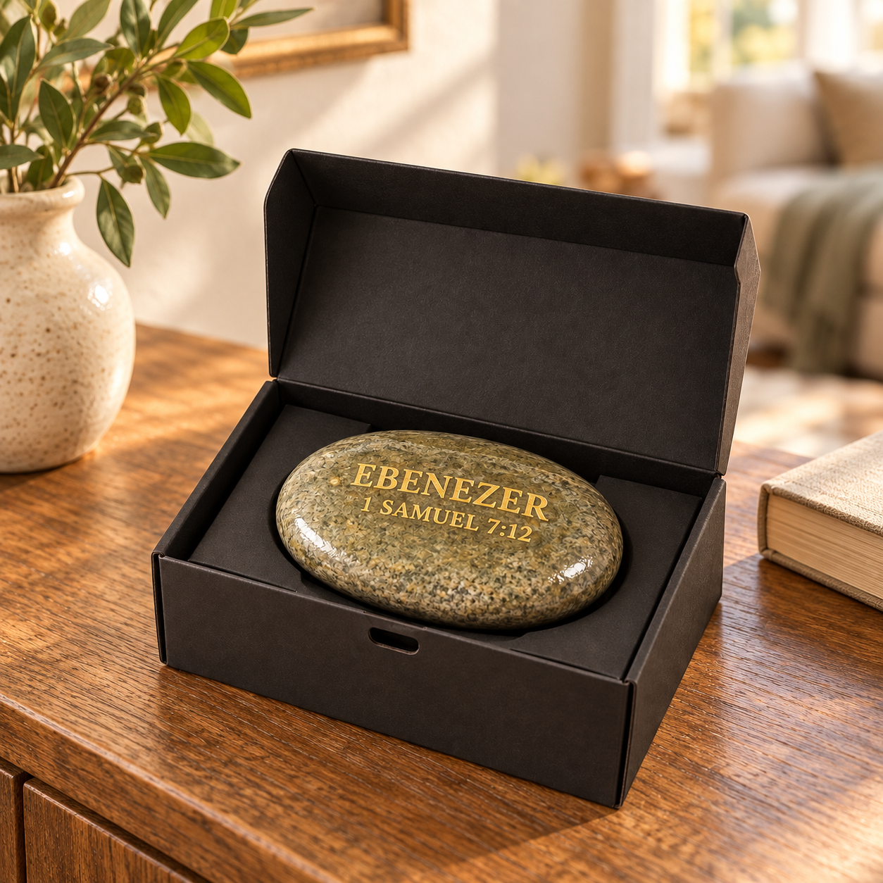 An EBENEZER Stone in its open black gift box on a sunlit wooden table at home